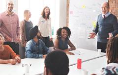 Man speaking to group around table in front of white board